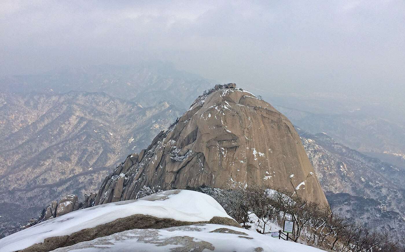 Snow on the Baegundae ridge with Insubong's granite dome and hazy ridgelines beyond in Bukhansan National Park